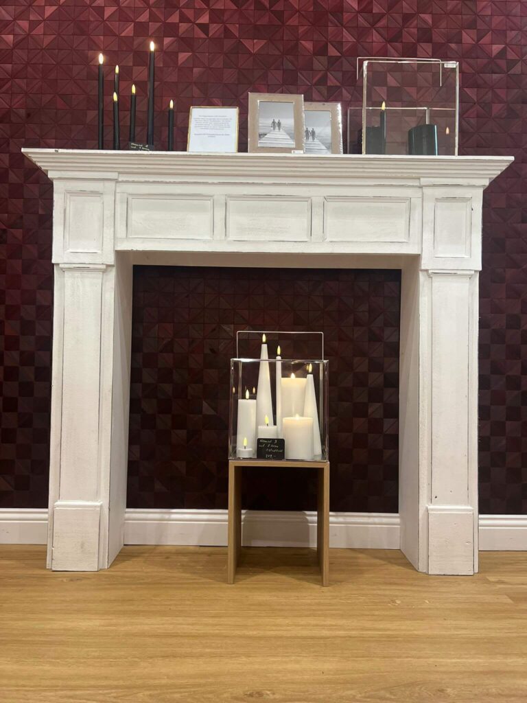 Dekorative Kaminumrandung mit Kerzen vor roter Wand.